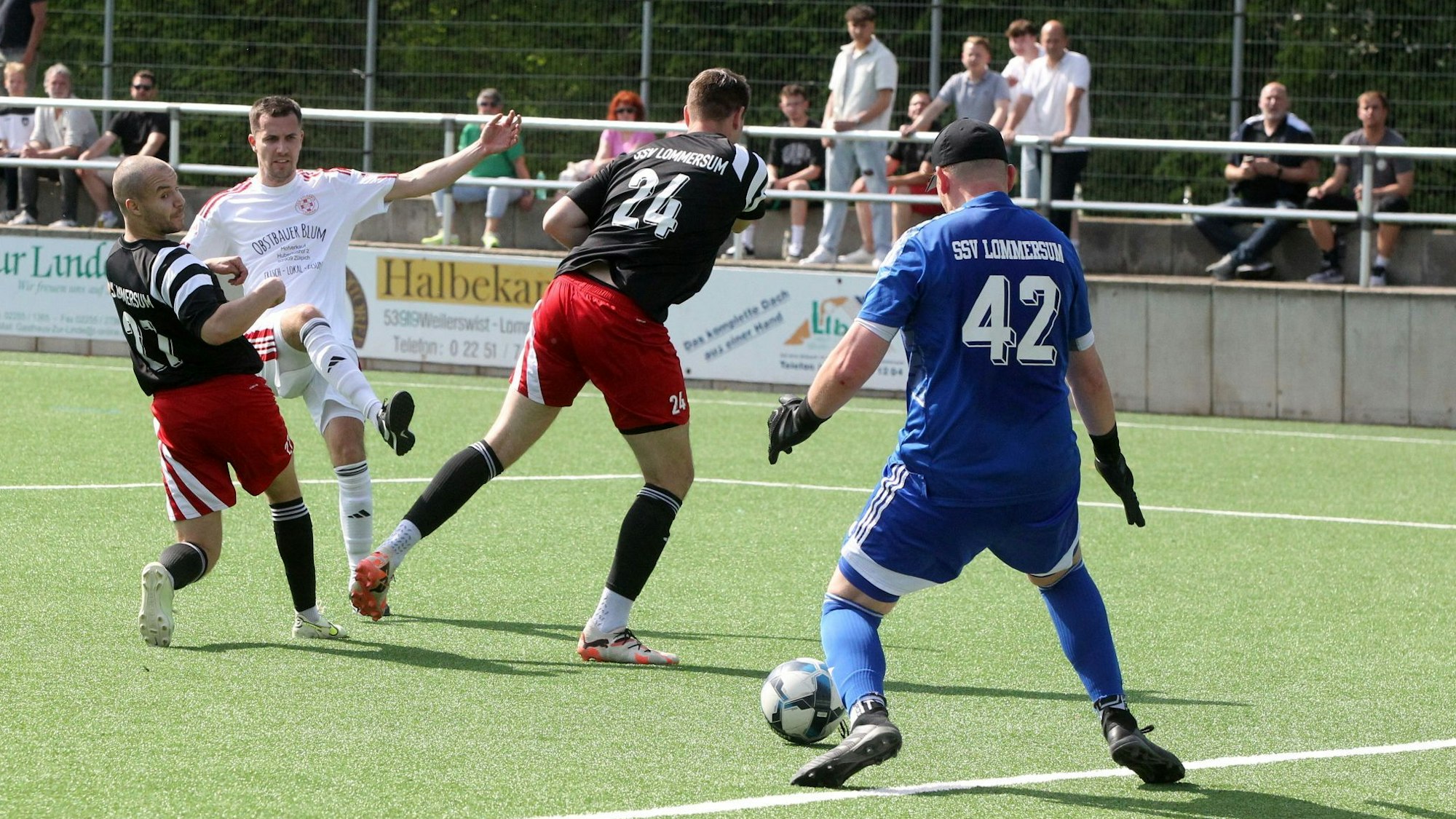 Ein Fußballer hat einen Ball geschossen, der durch die Beine der Verteidiger rutscht und vermutlich vom Torwart gehalten wird.