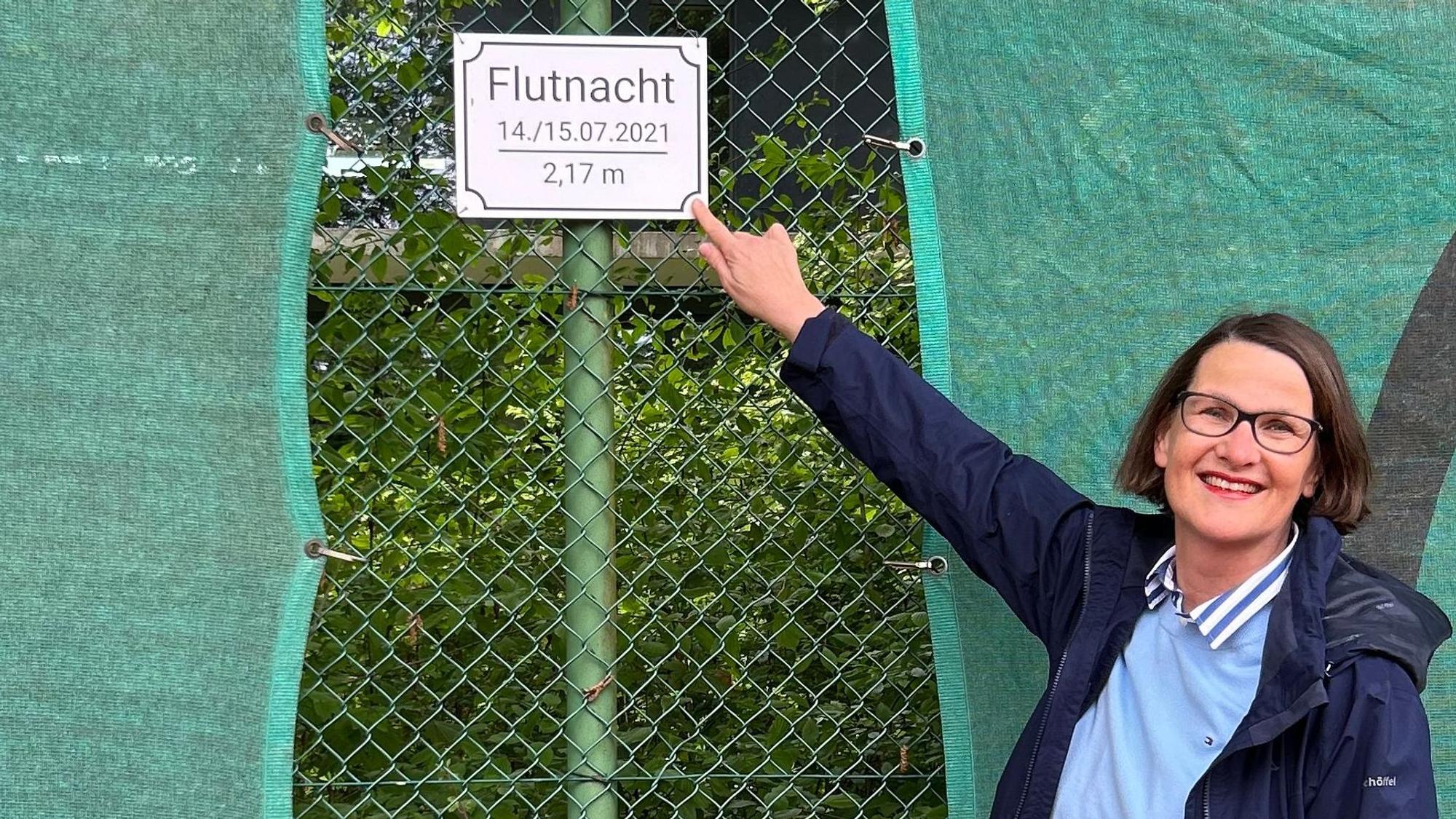 Angela Röthel, seit Februar 2025 Vorsitzende des Vereins, zeigt das Schild, das an die Hochwasserkatastrophe im Juli 2021 erinnert.