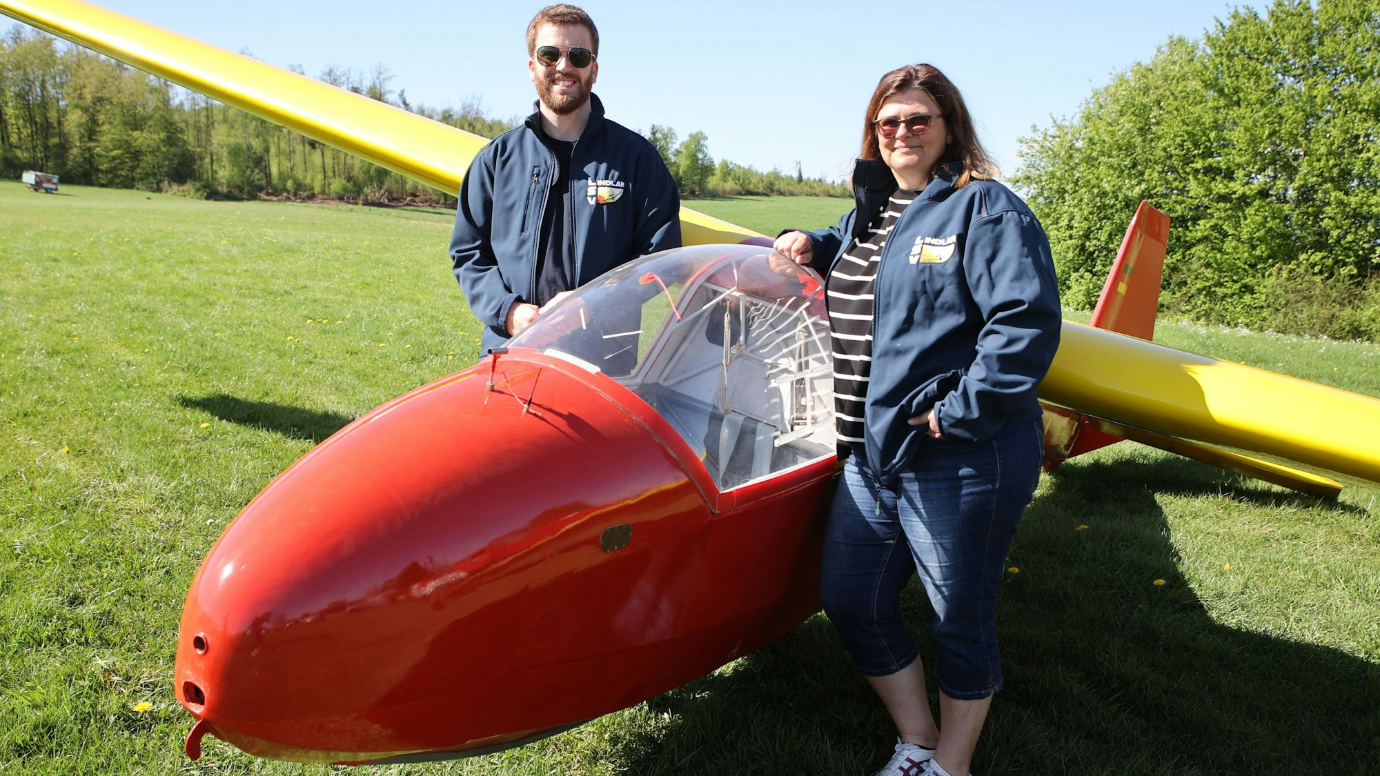 Ein Mann und eine Frau stehen vor einem roten Segelflugzeug.
