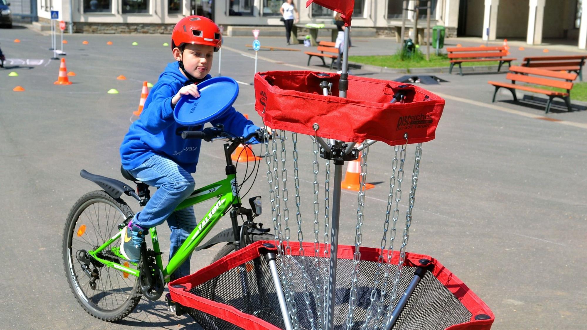 Ein Junge fährt auf dem Fahrrad und zielt mit deinem Frisbee auf einen Korb.