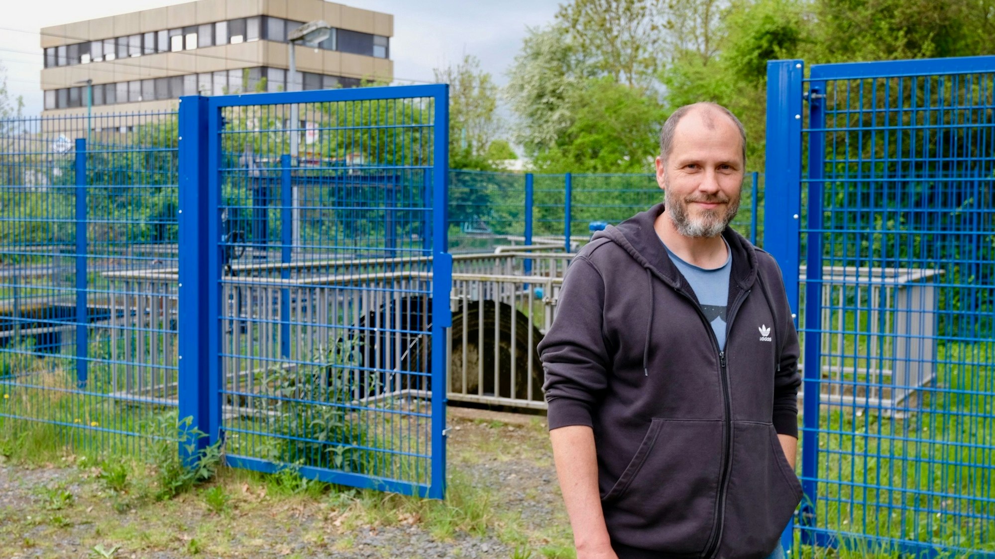 Ein Mann steht vor einer Schöpfanlage, die mit blauen Zäunen eingezäunt ist.