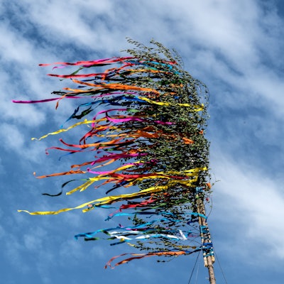 Bunte Bänder eines Maibaumes flattern vor dem blauen Himmel.
