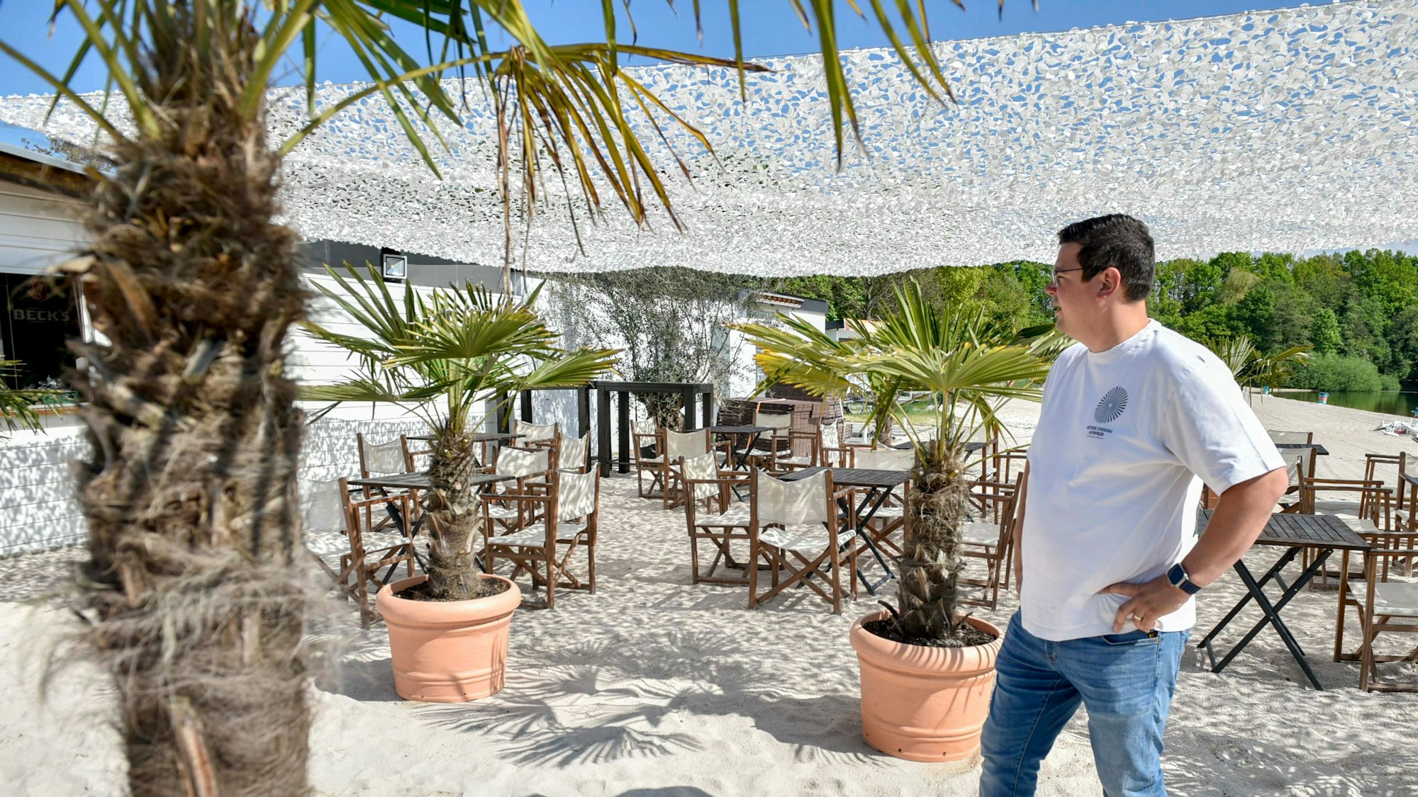 Zu sehen ist Christoph Hausmann, der im weißen Sand vor Töpfen mit Palmen steht.