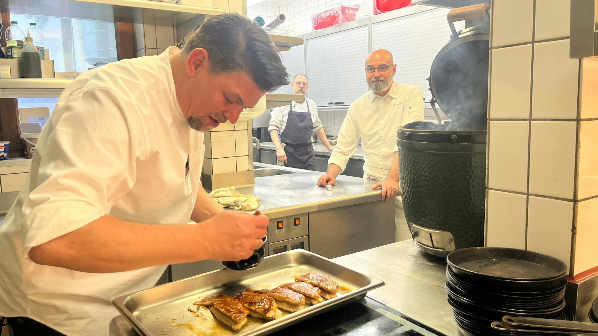 Eric Menchon schaut Tim Mälzer dabei zu, wie er die Rotbarbe glasiert. Menchon hat nur lobende Worte für den Fernsehkoch übrig.