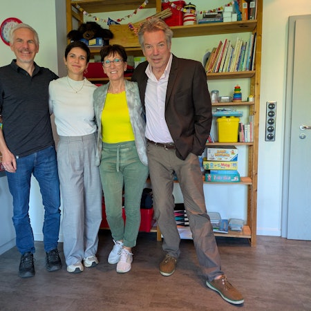 Zwei Männer und zwei Frauen stehen vor einem Regal mit Spielsachen und Kinderbüchern.
