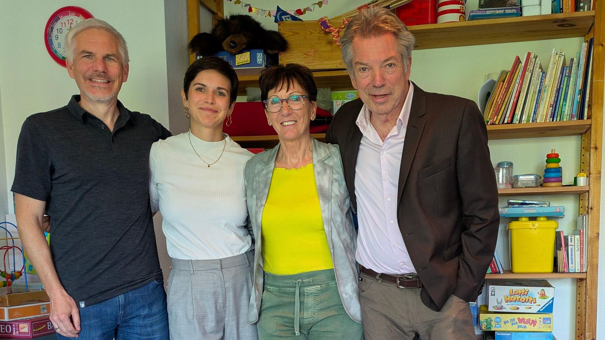 Zwei Männer und zwei Frauen stehen vor einem Regal mit Spielsachen und Kinderbüchern.