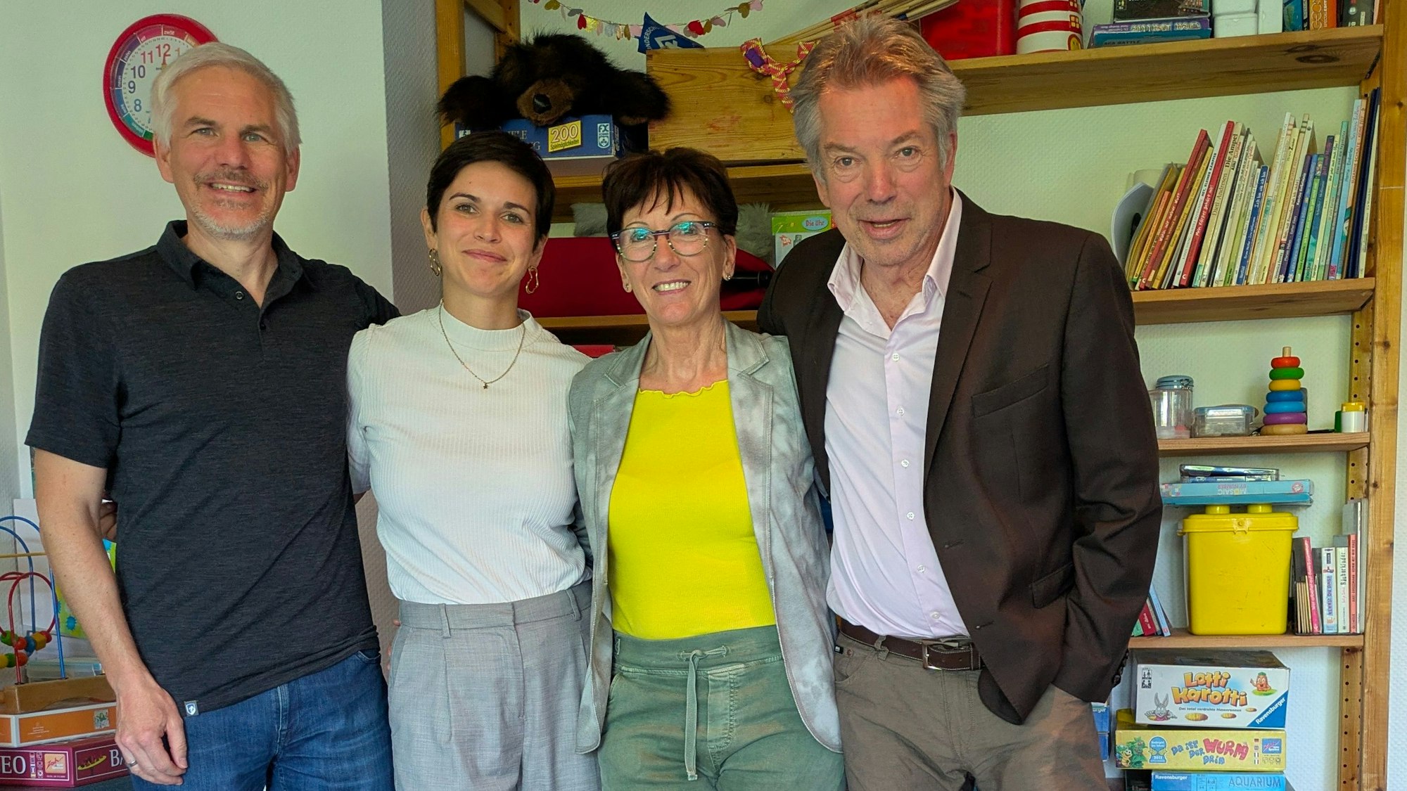 Zwei Männer und zwei Frauen stehen vor einem Regal mit Spielsachen und Kinderbüchern.