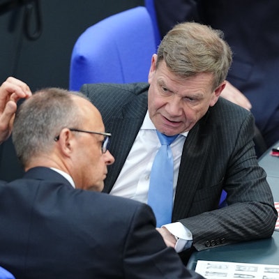 Zwei Politiker sitzen im Bundestag und sprechen miteinander.