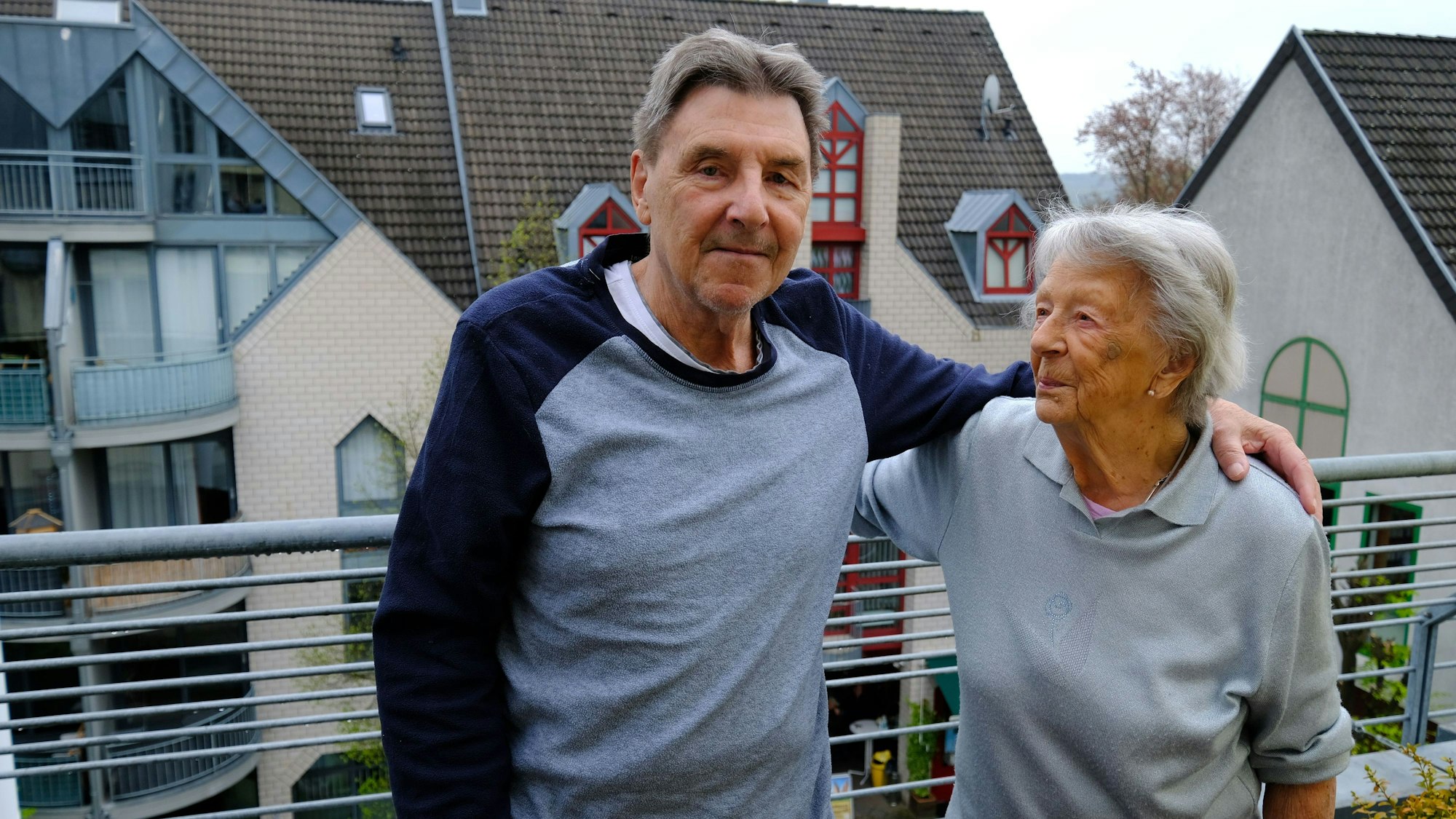 Das Foto zeigt Mutter und Sohn, die Arm in Arm auf einem Balkon stehen.