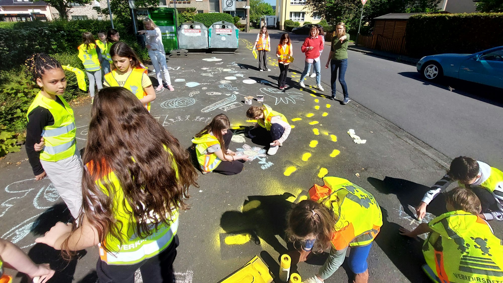 Kinder in Warnwesten bemalen einen Gehweg.