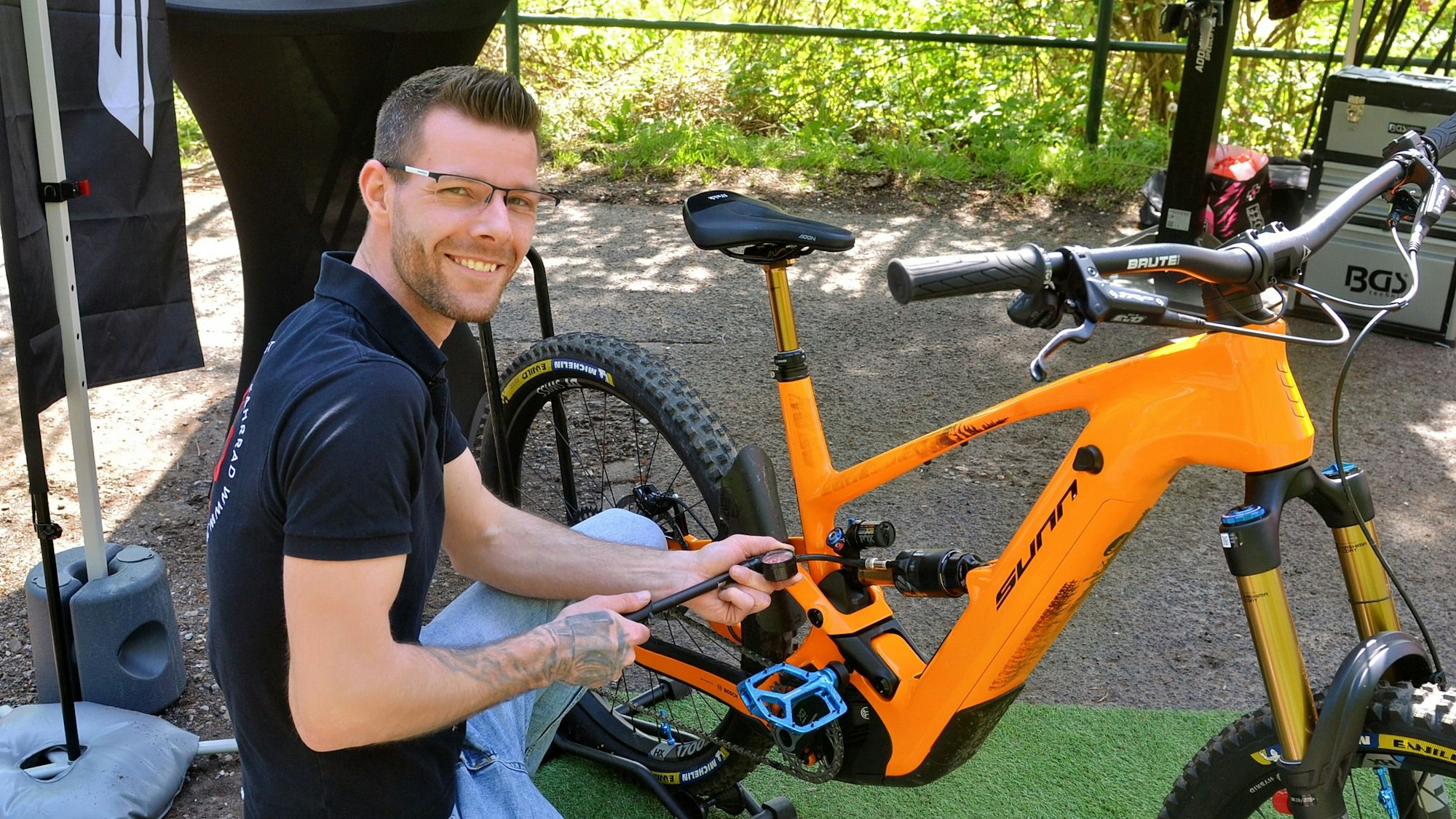 Das Bild zeigt einen Mechaniker, der neben einem Fahrrad hockt und daran arbeitet.