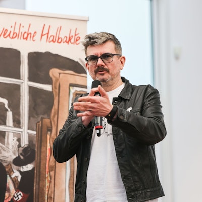28.04.2025, Nordrhein-Westfalen, Köln: Der französische Karikaturist Luz steht bei der Vorstellung seines Comics «Zwei weibliche Halbakte» vor dem gleichnamigen Bild im Museum Ludwig. Luz war viele Jahre lang einer der wichtigsten Karikaturisten von «Charlie Hebdo». In seinem neuen Comic erzählt er die Geschichte des Bildes «Zwei weibliche Halbakte» (1919) von Otto Mueller, das von den Nazis als «entartet» eingestuft wurde.
