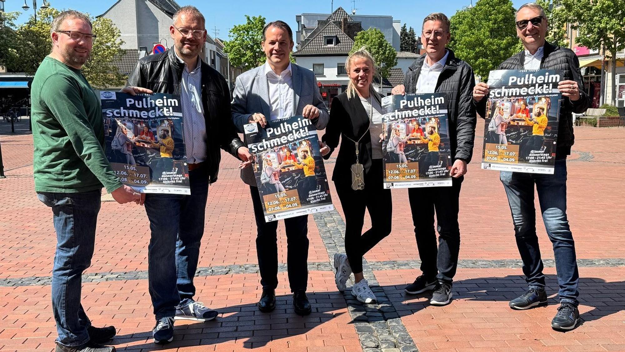 Eine Frau und fünf Männer halten Plakate mit der Aufschrift „Pulheim schmeckt “in die Kamera.