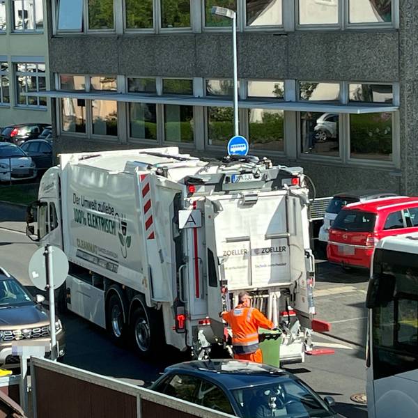 Ein elektrischer Müllwagen in Hennef. Ein Arbeiter rollt eine grüne Papiertonne zum Fahrzeug.