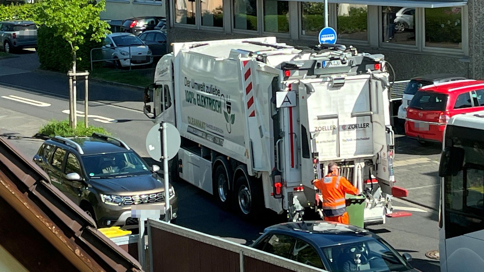 Ein elektrischer Müllwagen in Hennef. Ein Arbeiter rollt eine grüne Papiertonne zum Fahrzeug.