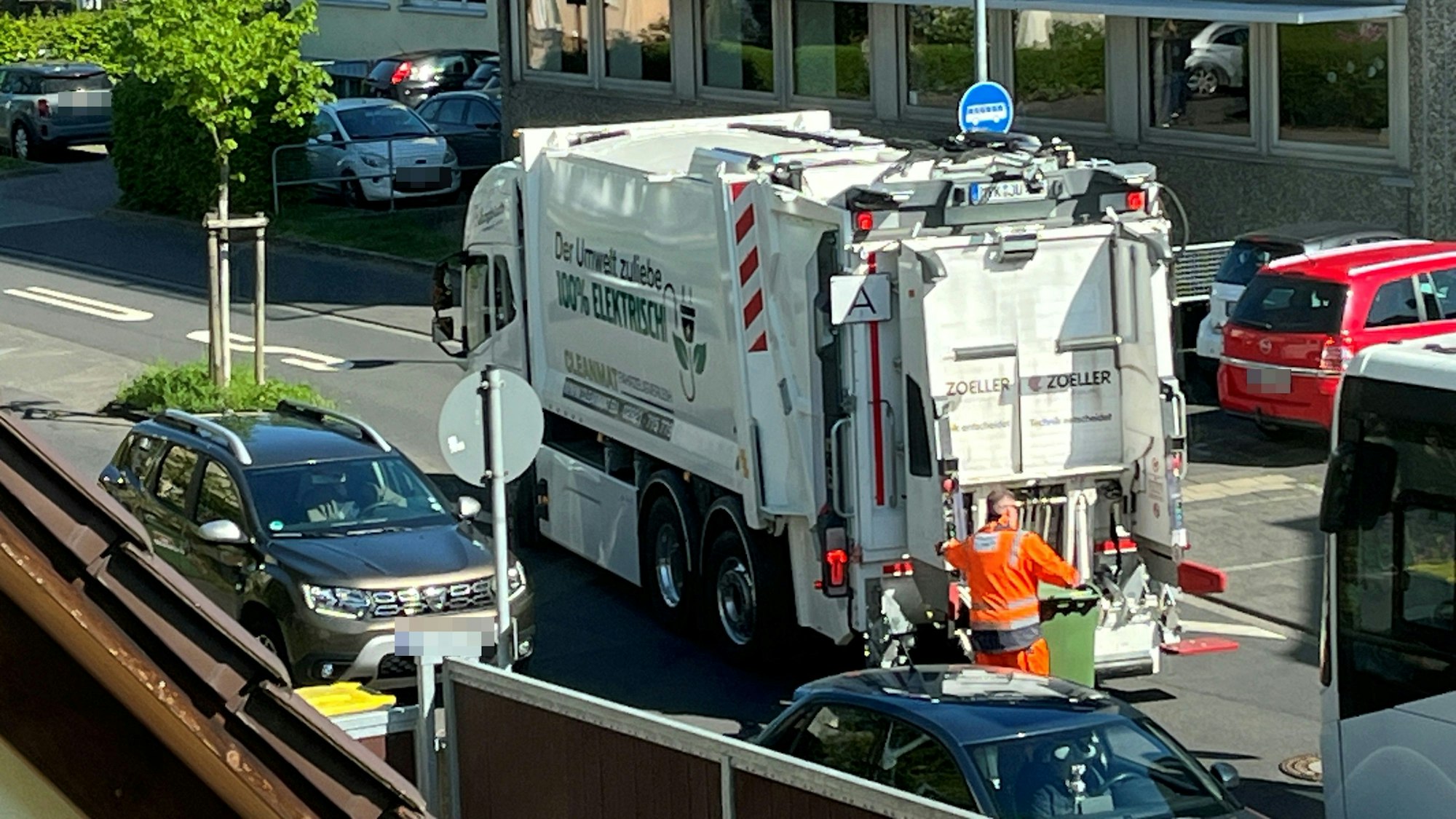 Ein elektrischer Müllwagen in Hennef. Ein Arbeiter rollt eine grüne Papiertonne zum Fahrzeug.