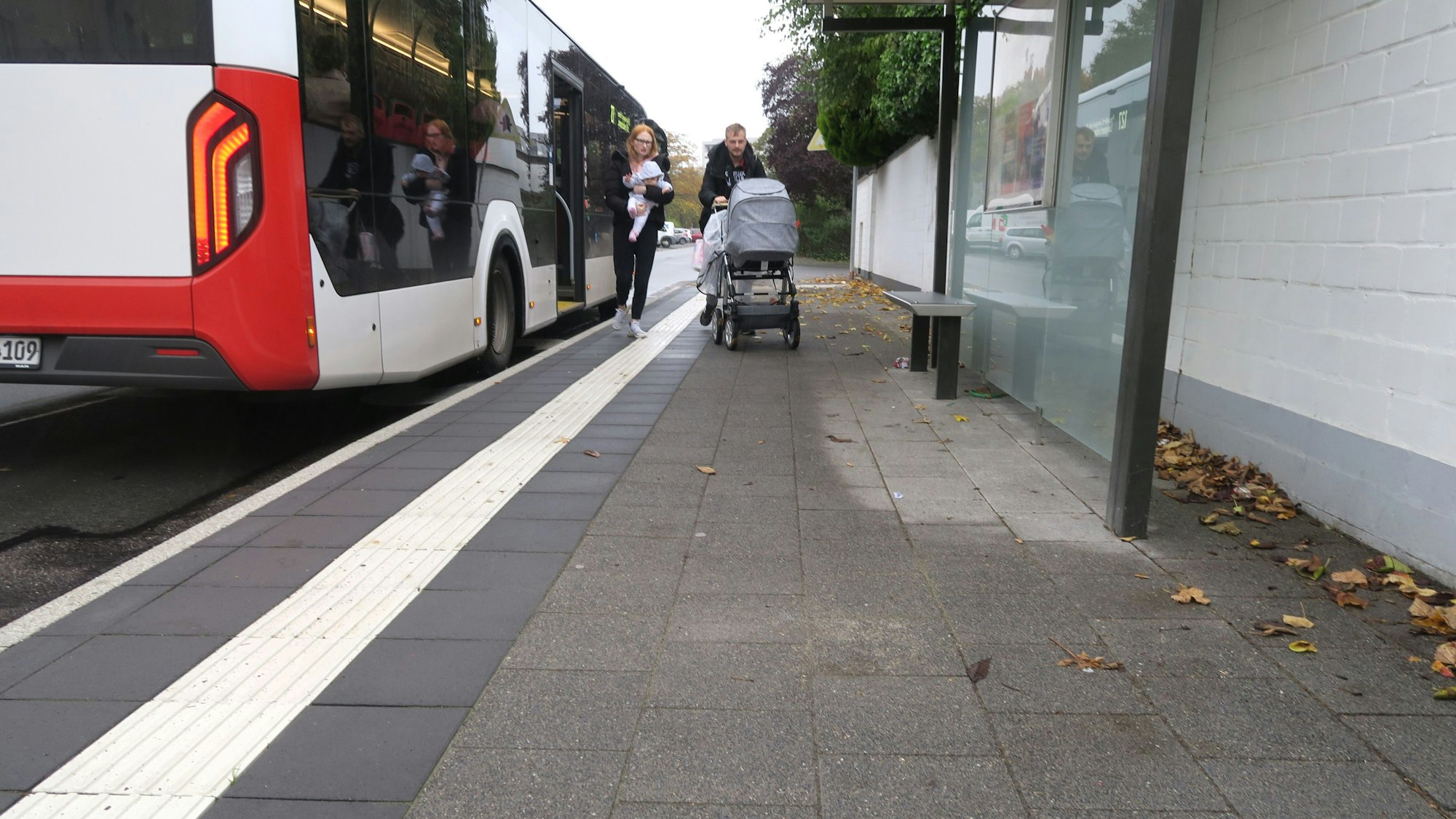 Ein Bus steht an einer Haltestelle, ein Paar mit Kinderwagen ist gerade ausgestiegen.