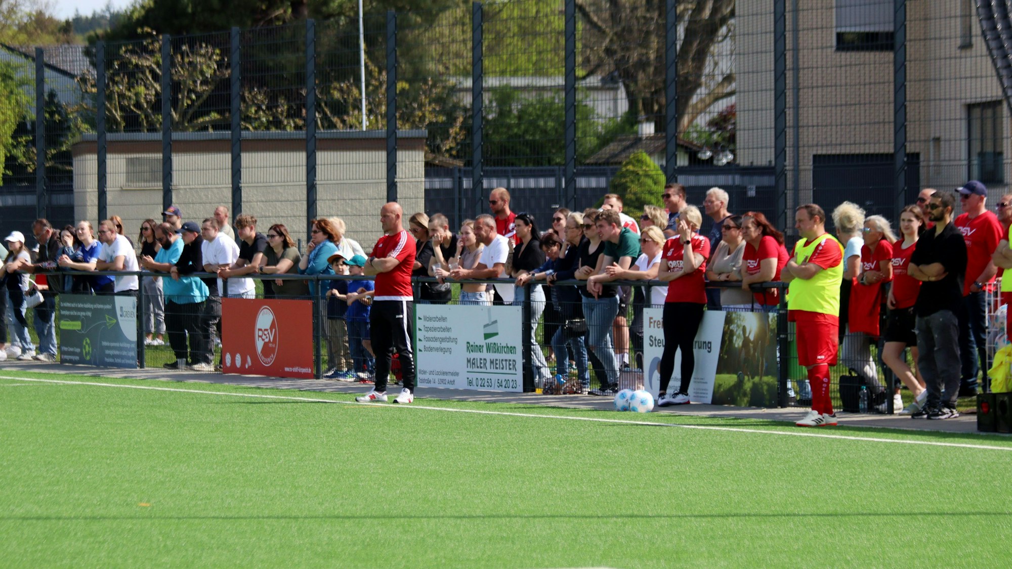 Hinter dem Zaun stehen Dutzende Zuschauer, die das Kreisliga-C-Spiel verfolgen.