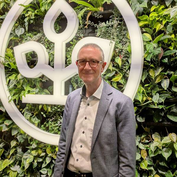 Helmut Schneider steht vor einer begrünten Wand mit einem AOK-Emblem.