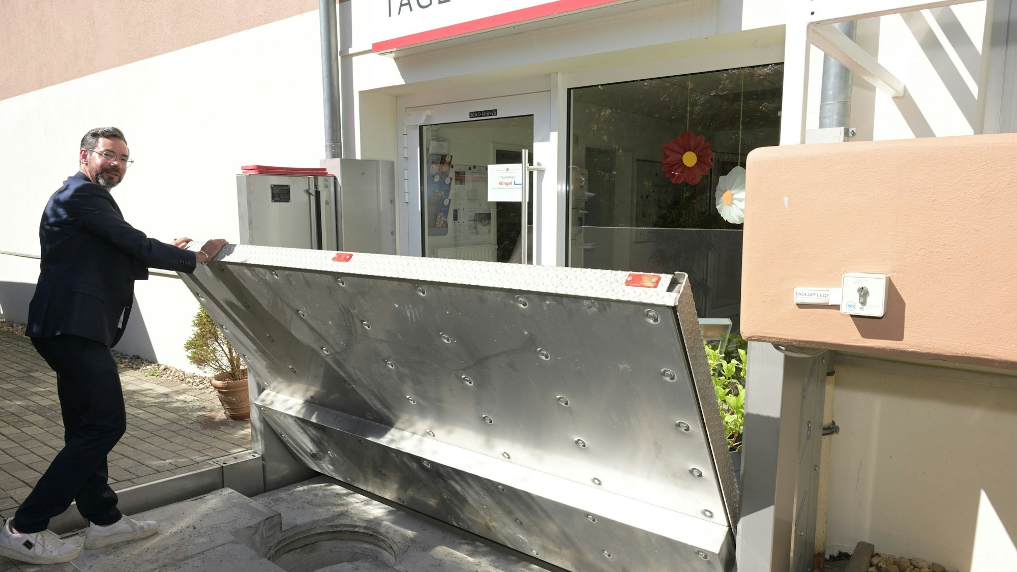 Vor der Tagespflege des Wöllner-Stifts in Rösrath-Hoffnungsthal zeigt Geschäftsführer Michael Heine, wie eine Edelstahl-Wand im Fall von Hochwasser automatisch hochgefahren wird.