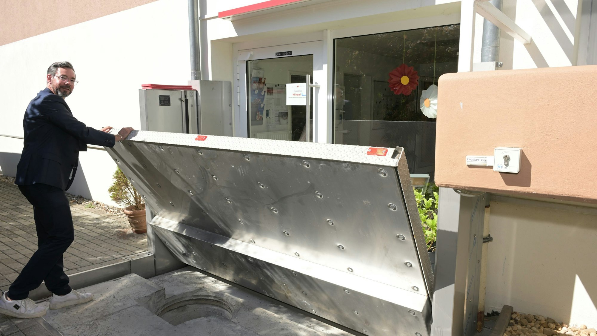 Vor der Tagespflege des Wöllner-Stifts in Rösrath-Hoffnungsthal zeigt Geschäftsführer Michael Heine, wie eine Edelstahl-Wand im Fall von Hochwasser automatisch hochgefahren wird.