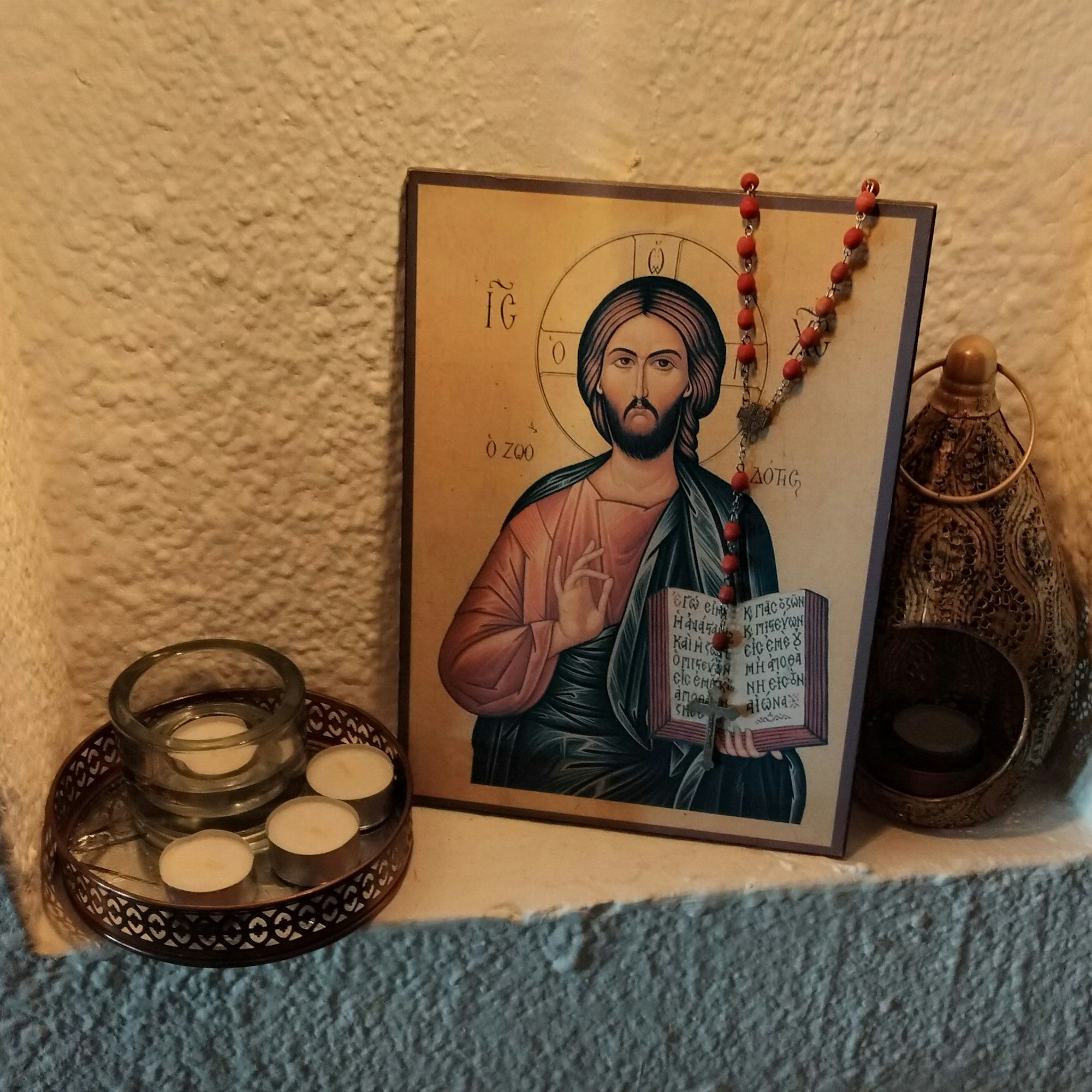 Ein Bild von Jesus, mit Rosenkranz und Kerzen steht in einer Nische