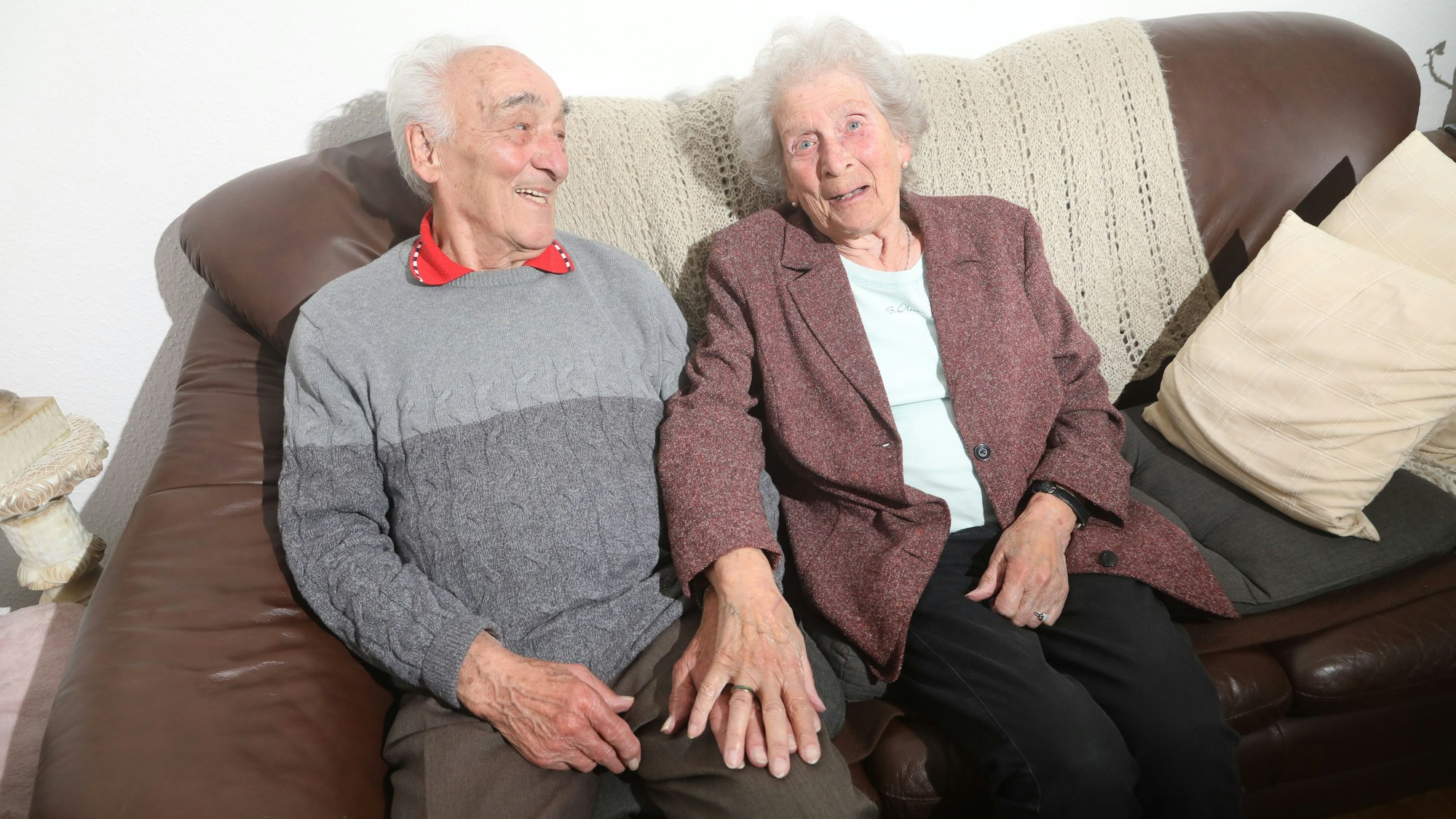 Ein älteres Ehepaar sitzt auf einer braunen Couch.