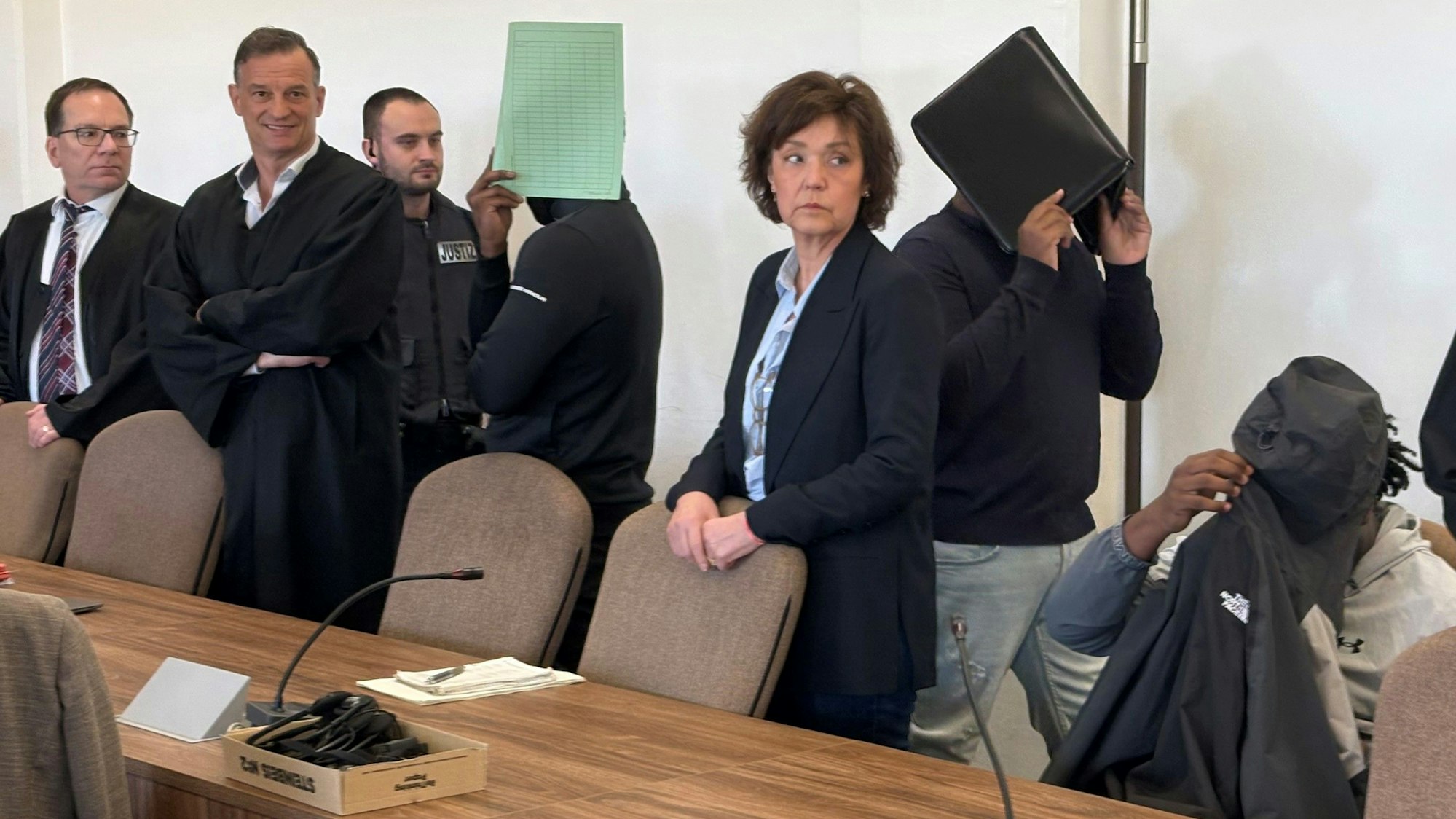 Die drei Angeklagten mit Verteidigern, Dolmetscherin und Wachtmeister beim Prozess im Kölner Landgericht