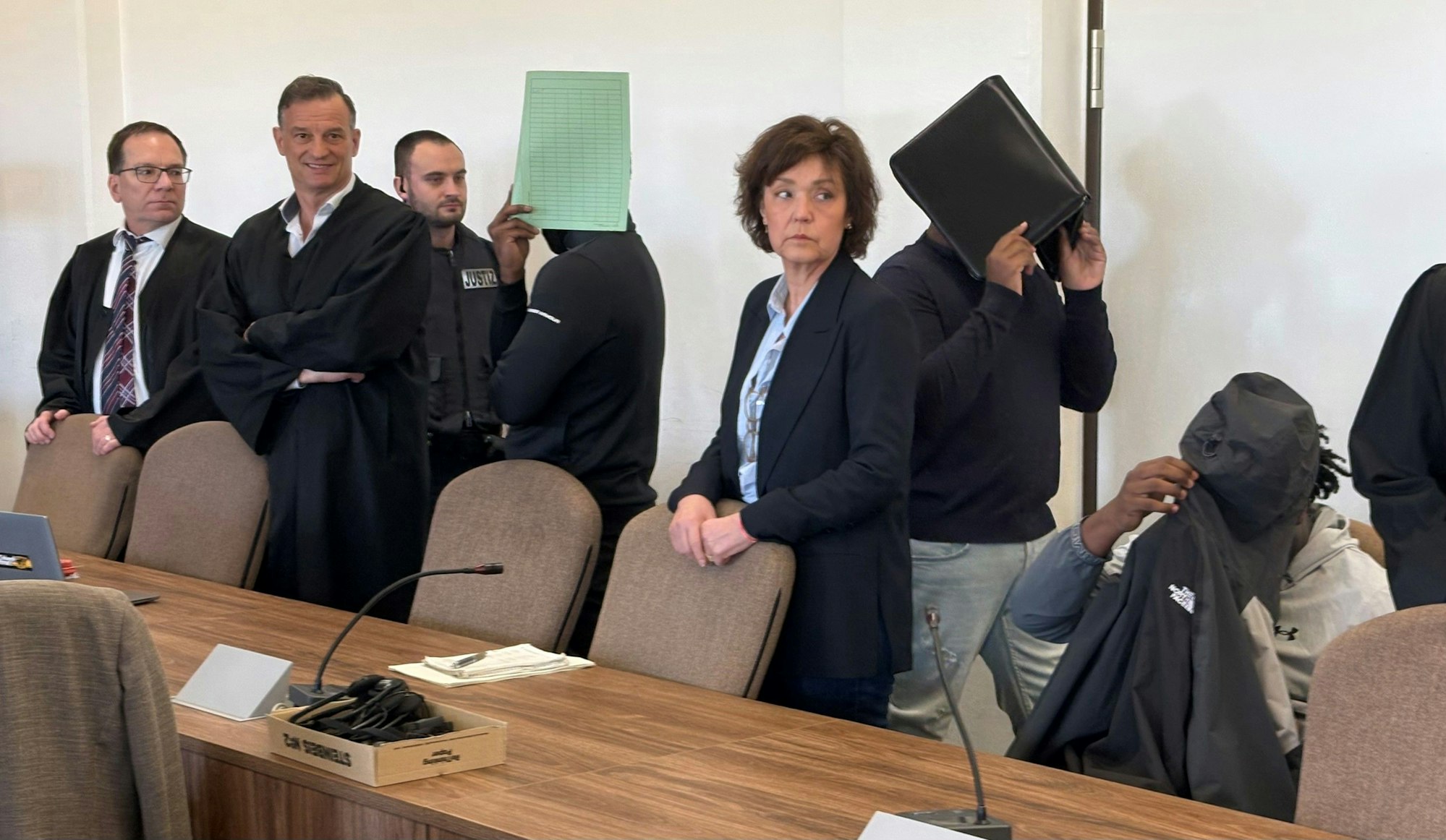 Die drei Angeklagten mit Verteidigern, Dolmetscherin und Wachtmeister beim Prozess im Kölner Landgericht