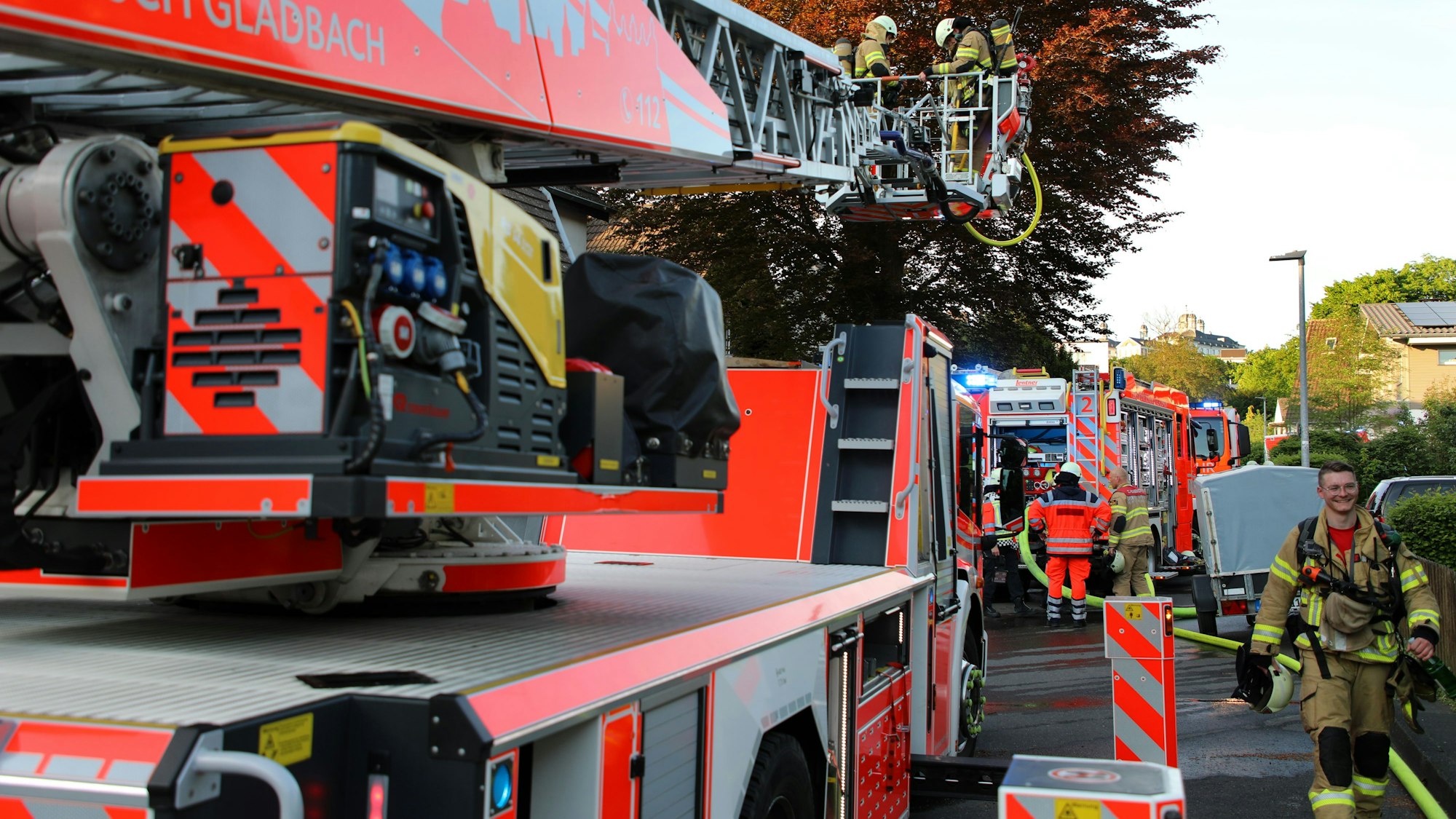 Feuerwehrfahrzeuge stehen in einer Straße, Feuerwehrleute gehen dazwischen hindurch. Am Horizont ist Schloss Bensberg zu sehen.
