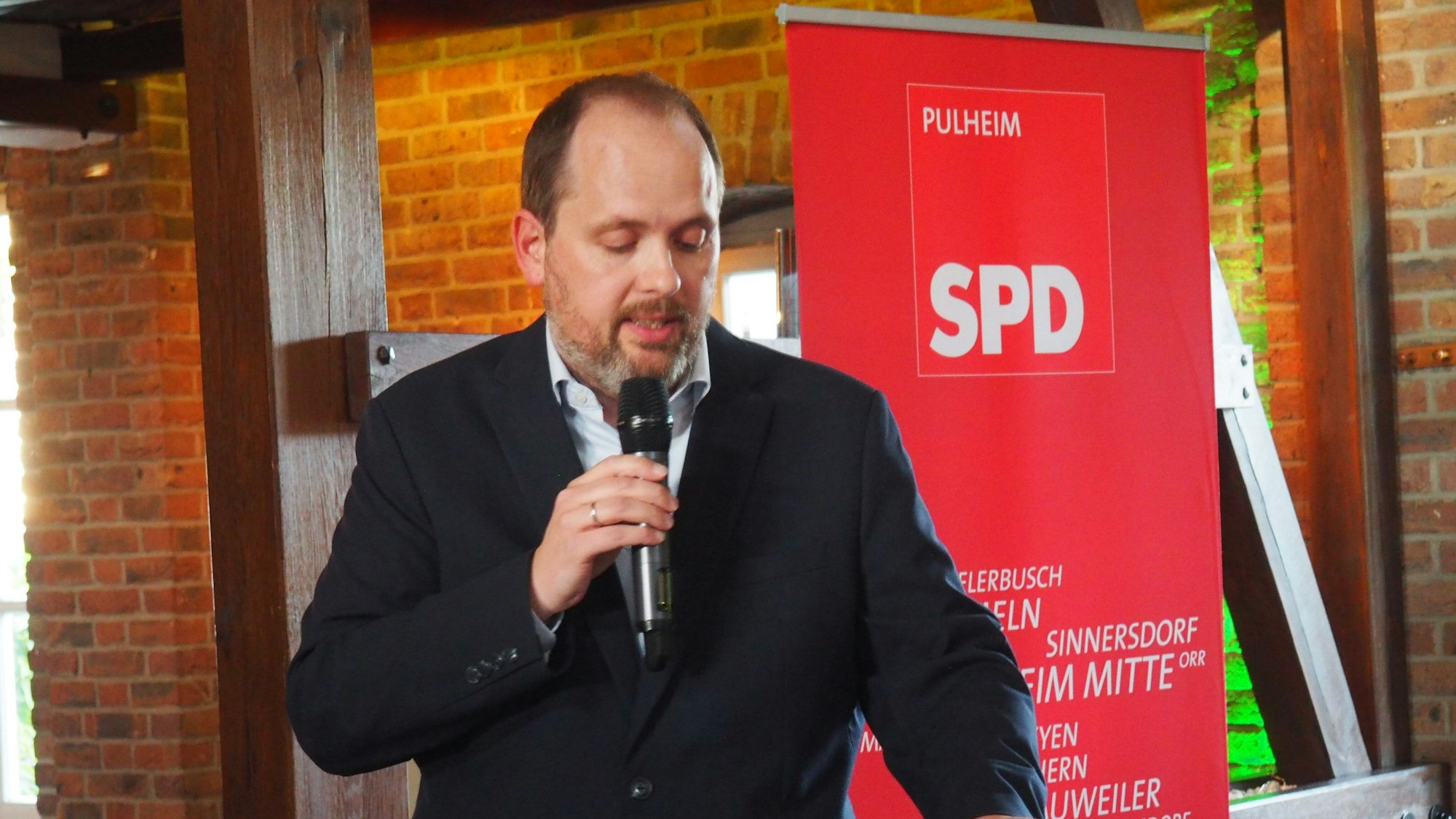 Ein Mann steht an einem Rednerpult, in der Hand hält er ein Mikrofon, im Hintergrund steht ein Schild mit dem Schriftzug SPD.