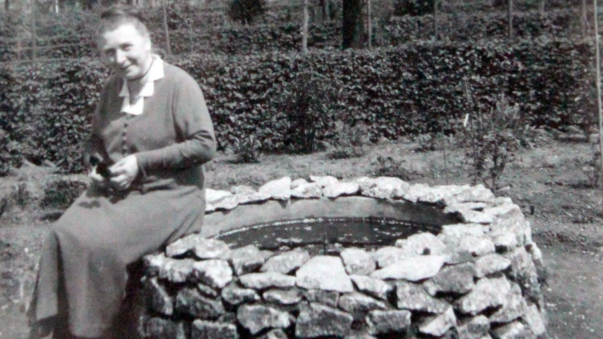 Chistine Jung sitzt in ihrem Garten auf dem Rand eines Brunnens und lächelt in die Kamera. Das Bild ist 1934 aufgenommen worden.