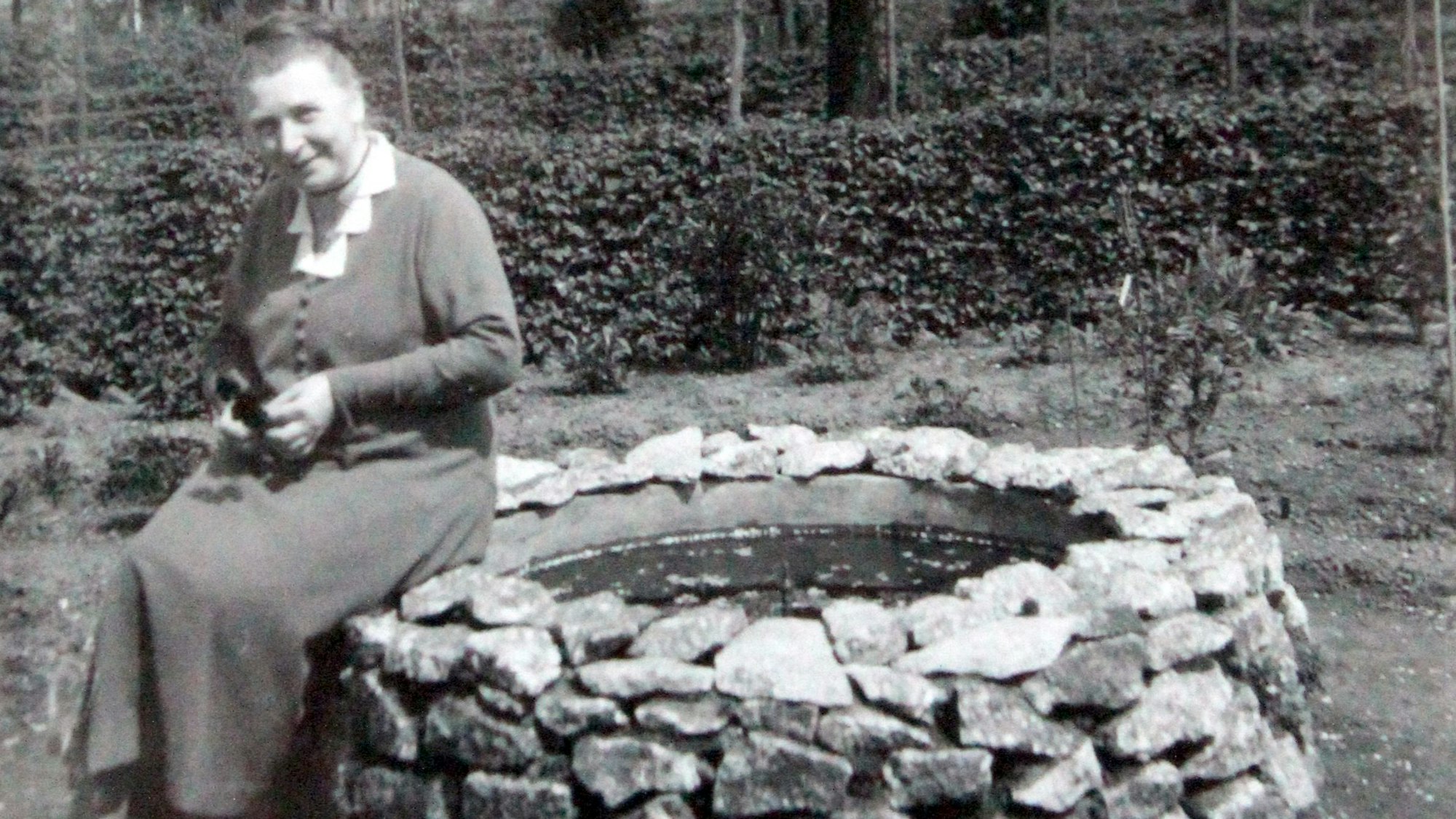 Chistine Jung sitzt in ihrem Garten auf dem Rand eines Brunnens und lächelt in die Kamera. Das Bild ist 1934 aufgenommen worden.