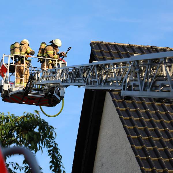 Feuerwehrleute inspizieren vom Korb einer Drehleiter aus ein Hausdach.