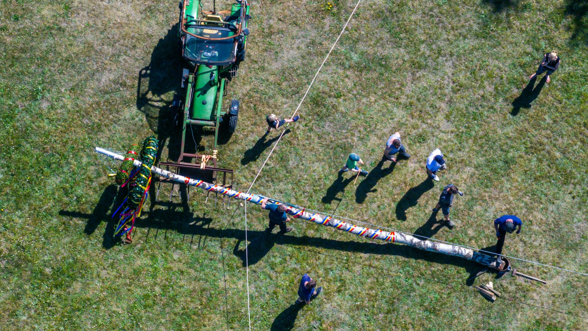 Mitglieder der Freiwilligen Feuerwehr und der Traktortruppe Pokrent (Mecklenburg-Vorpommern stellen am Dorfteich den traditionellen Maibaum auf.