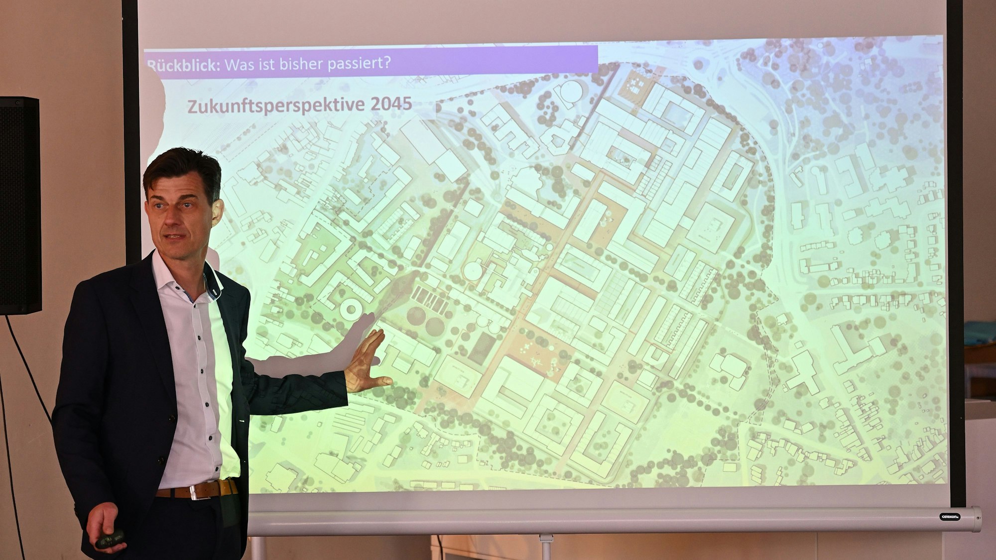 Oliver Brügge steht vor einer Leinwand ., wo ein Plan vom Zanders-Gelände abgebildet ist.