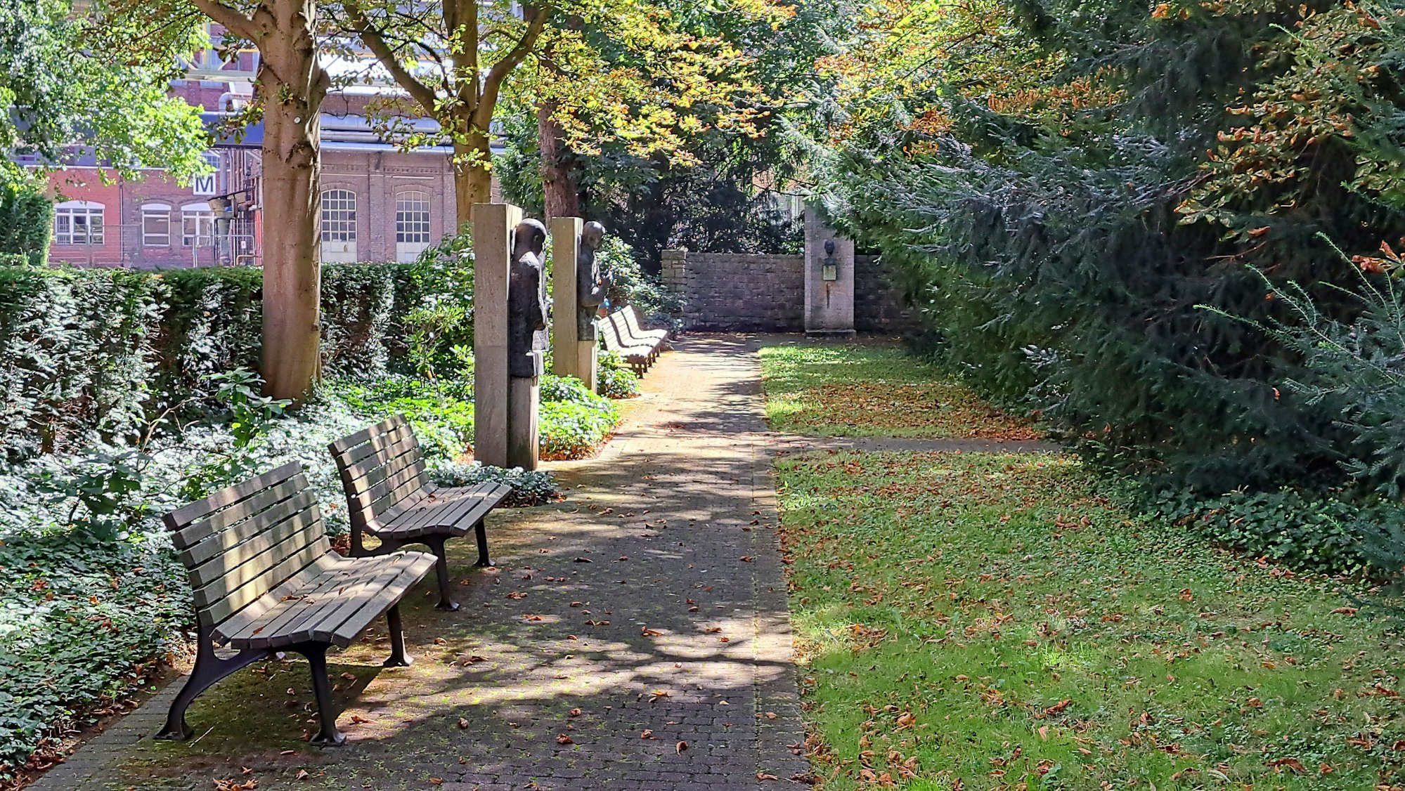 Ein Stück Wiese ist zu sehen, davor verläuft ein Weg, an dem Bänke stehen.
