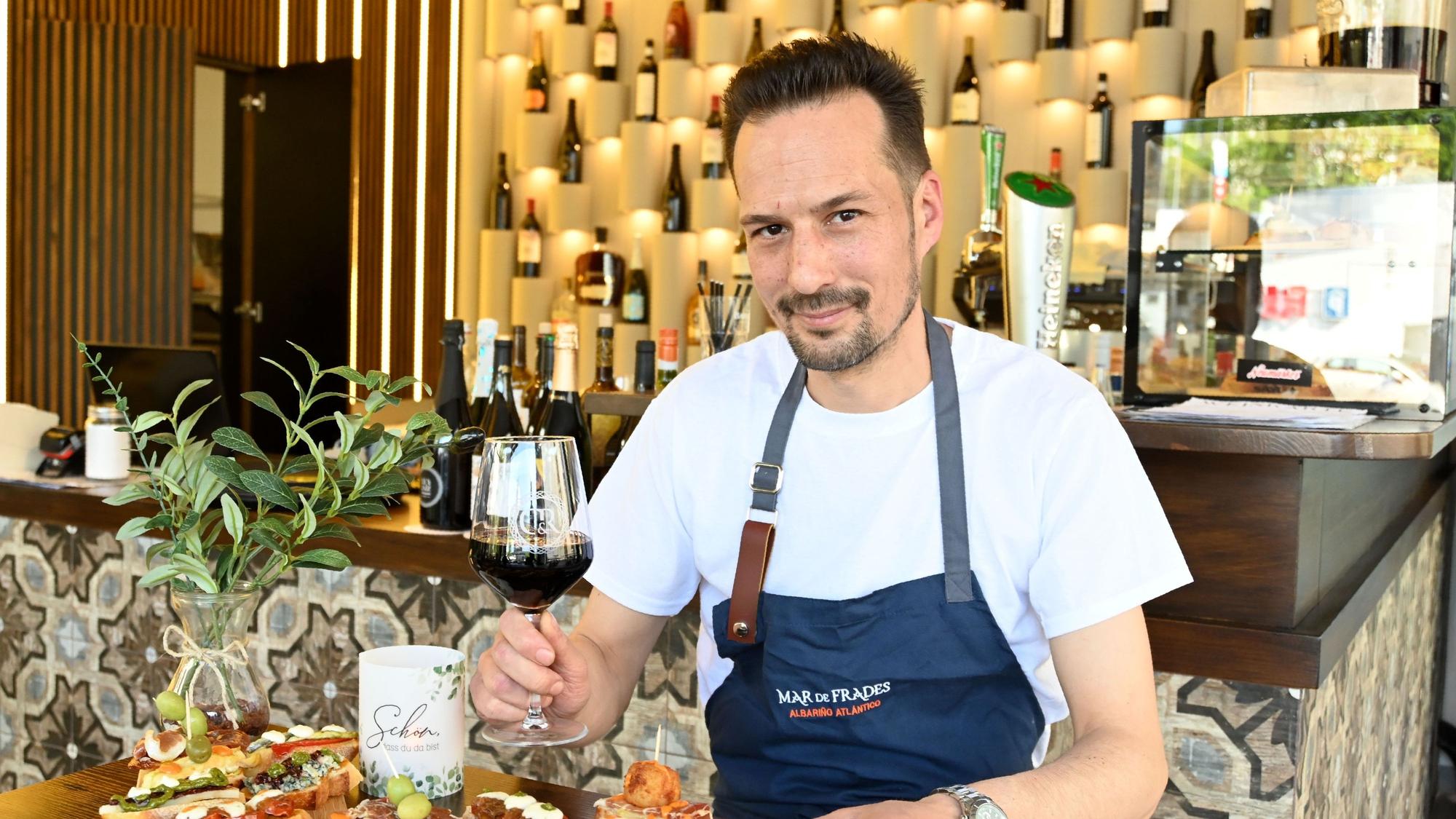 Ein Mann mit Wein in der Hand schaut in die Kamera.