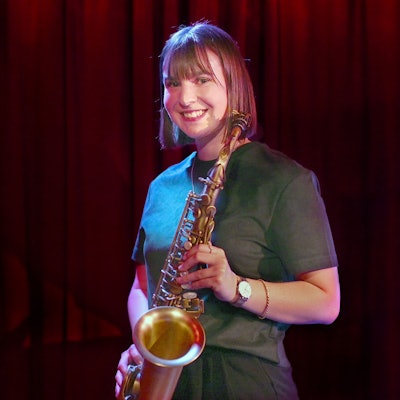 Paul Steimer trägt ein grünes Oberteil und hält ihr Saxofon.