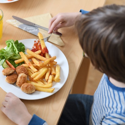 Ein Kind isst Pommes mit Fleisch: Der designierte Agrarminister Alois Rainer hat eine Debatte über Fleisch auf den Speiseplänen von Kitas und Schulen ausgelöst. (Archivbild)
