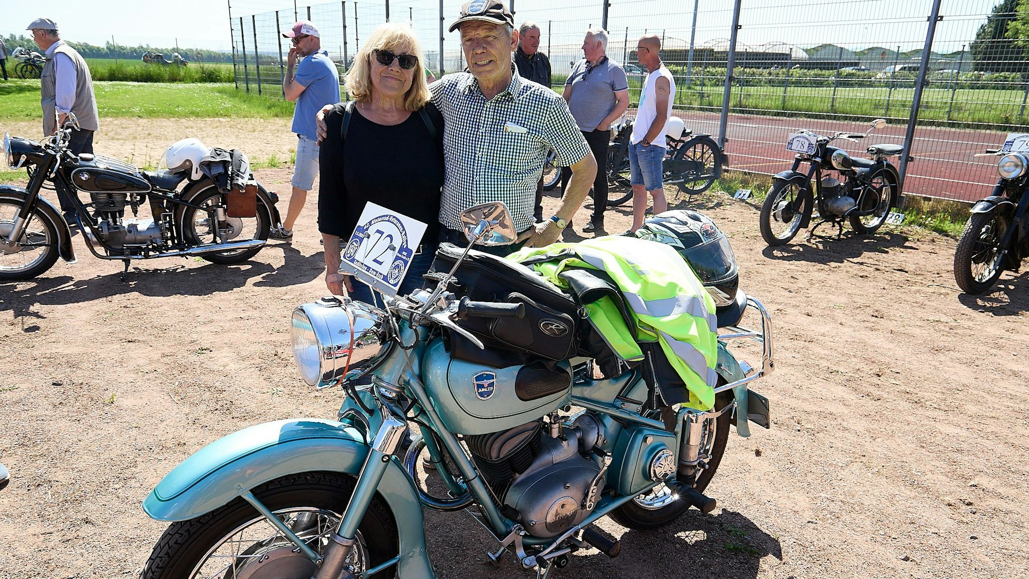 Die beiden stehen Arm in Arm hinter einem Motorrad.