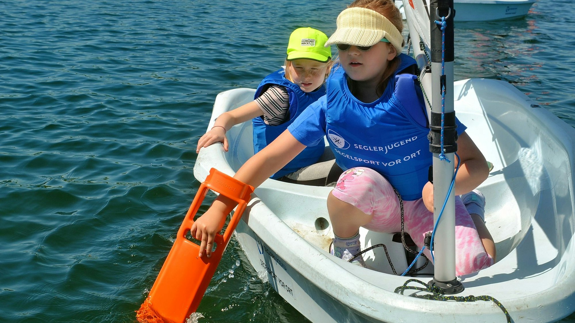 Die beiden Kinder sitzen im Boot. Eines versucht, das Boot mit einem Paddel fortzubewegen.