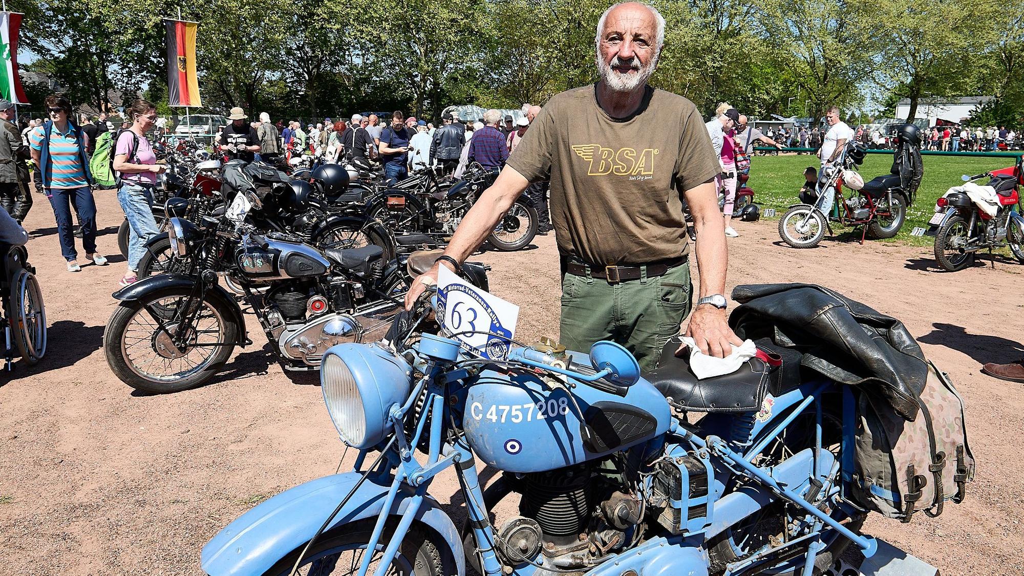 Im braunen T-Shirt steht Werner Wolff hinter einem hellblauen Motorrad.