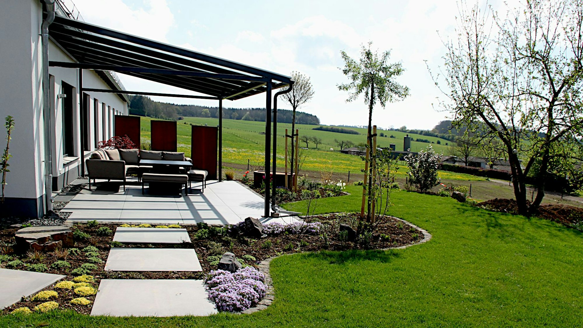 An ein Haus, das am linken Bildrand zu erkennen ist, grenzen eine Terrasse und ein Garten an.