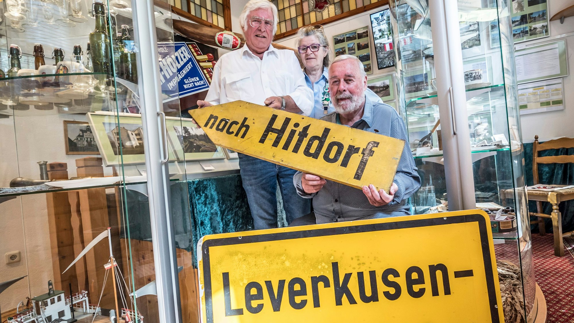 Vor 50 Jahren kam Hitdorf zu Leverkusen. Der Heimatverein Hitdorf erinnert an die Gebietsreform 1975 . Von links: Bernd Bilitzki hält ein altes Holzschild, ohne den Zusatz "Leverkusen", Marianne Fuchs-Biliki und vorne Klaus Roth. Foto: Ralf Krieger