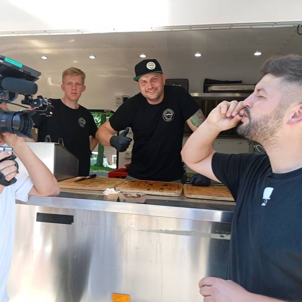 Das Foto zeigt einen Kameramann bei der Arbeit vor einem Imbisswagen.