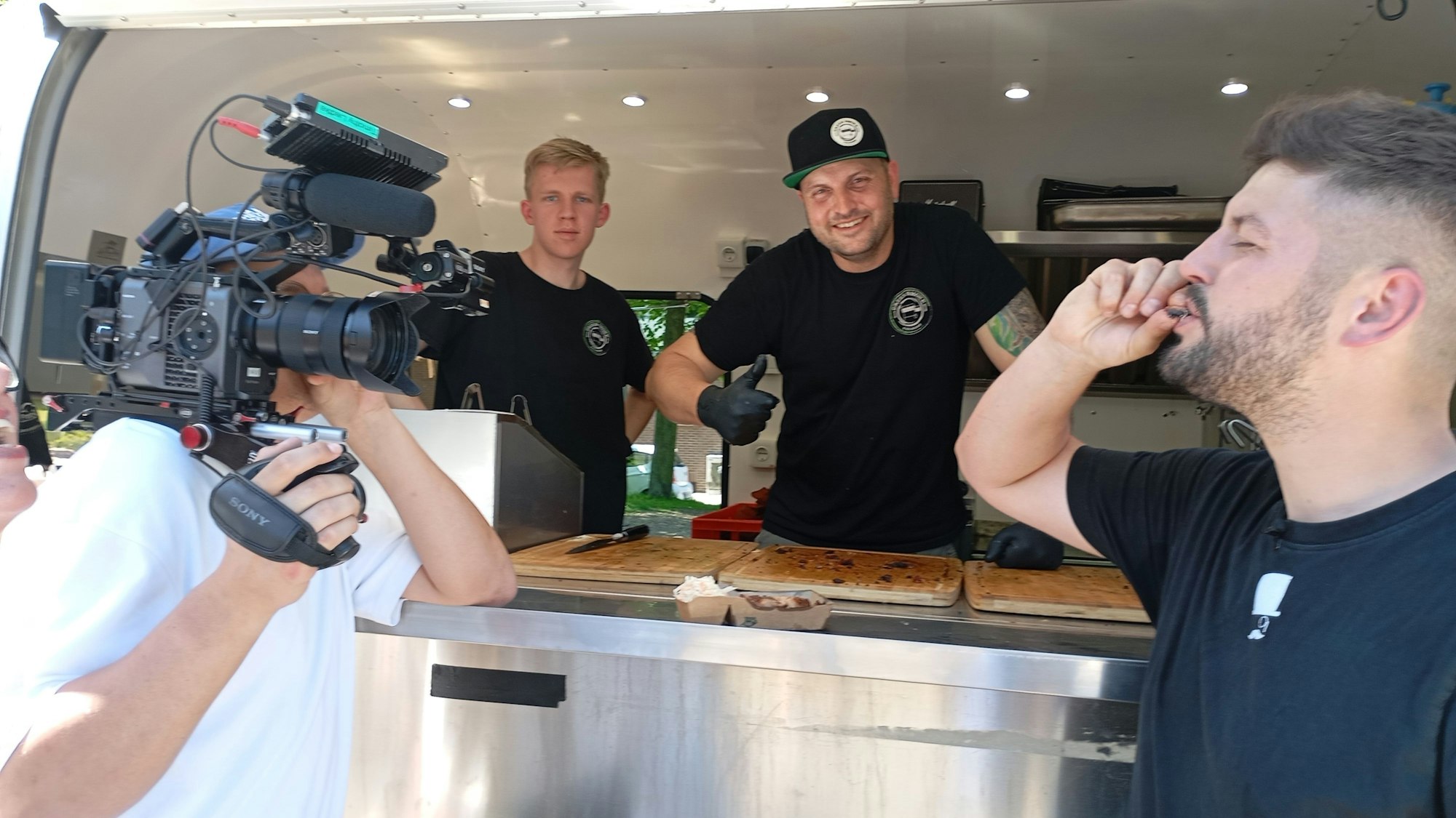 Das Foto zeigt einen Kameramann bei der Arbeit vor einem Imbisswagen.