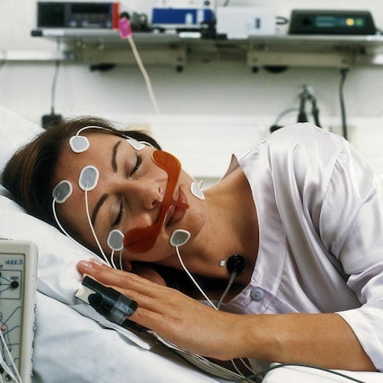 Auf dem Bild ist eine Patientin zu sehen, die verkabelt in einem Schlaflabor schläft.