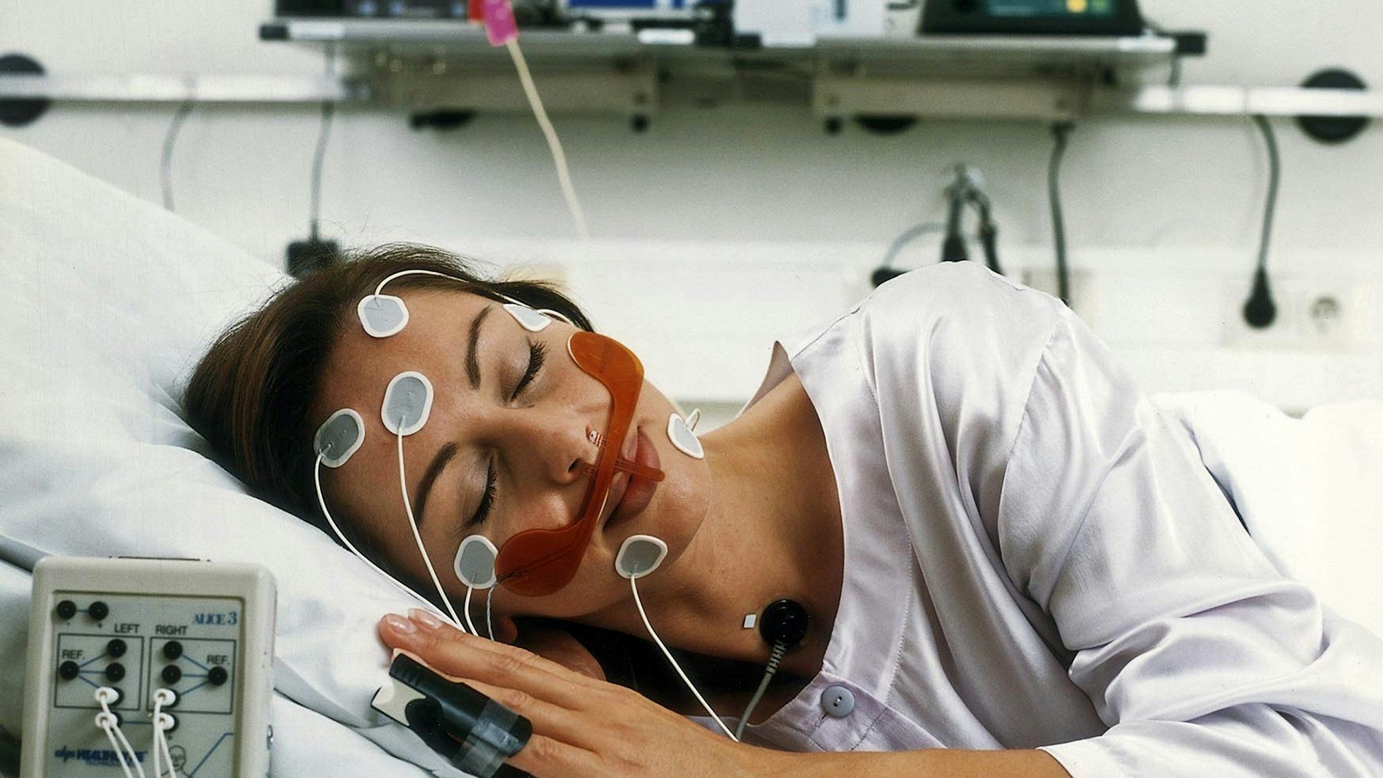 Auf dem Bild ist eine Patientin zu sehen, die verkabelt in einem Schlaflabor schläft.