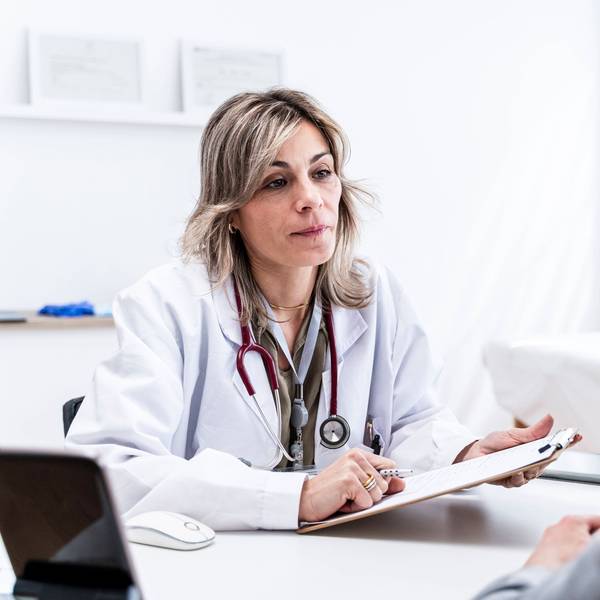 Eine Ärztin sitzt im Behandlungszimmer einer Praxis und hört ihrem Patienten zu